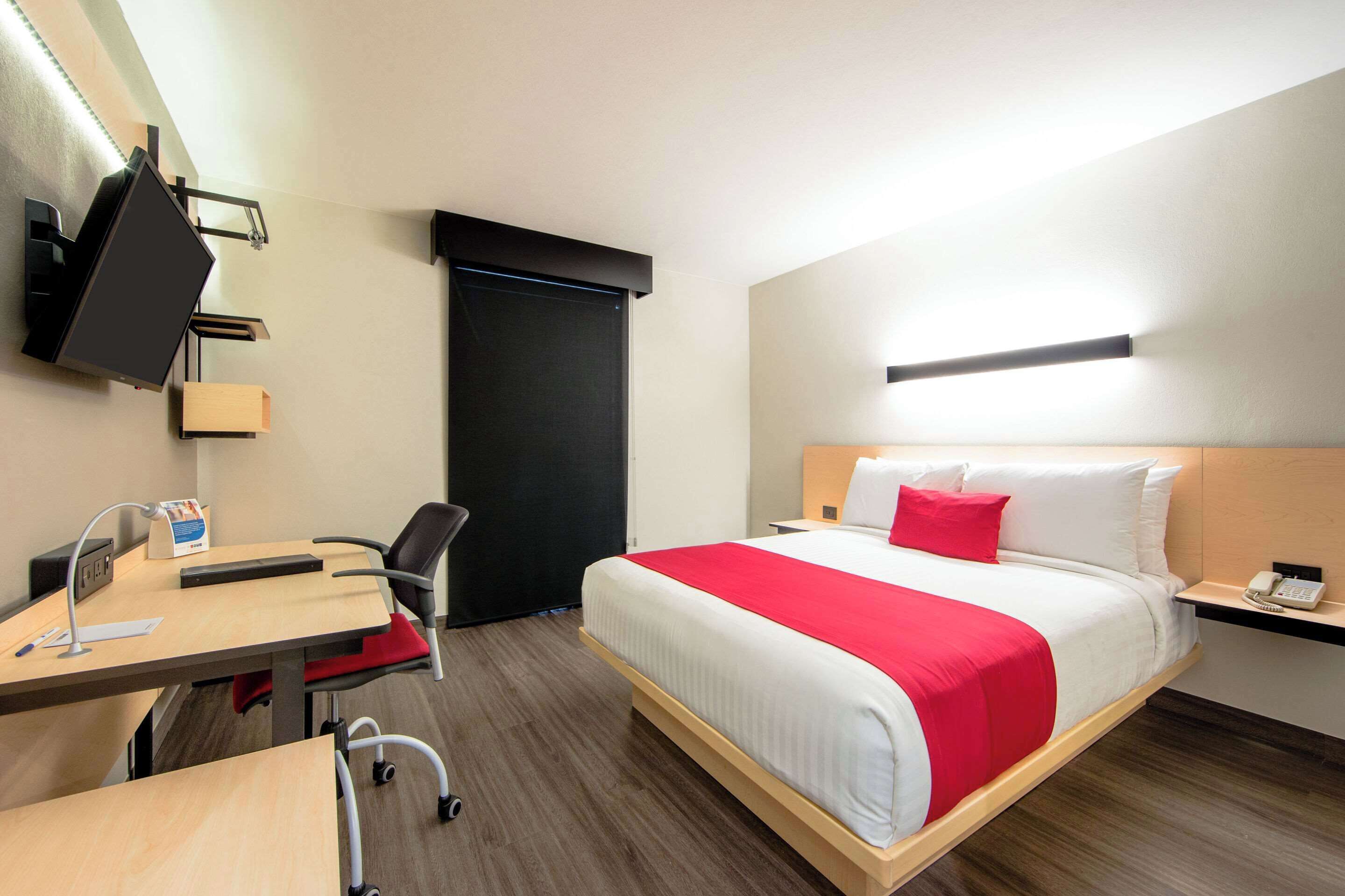 A hotel room with a bed, desk, chair, and a TV mounted on the wall.