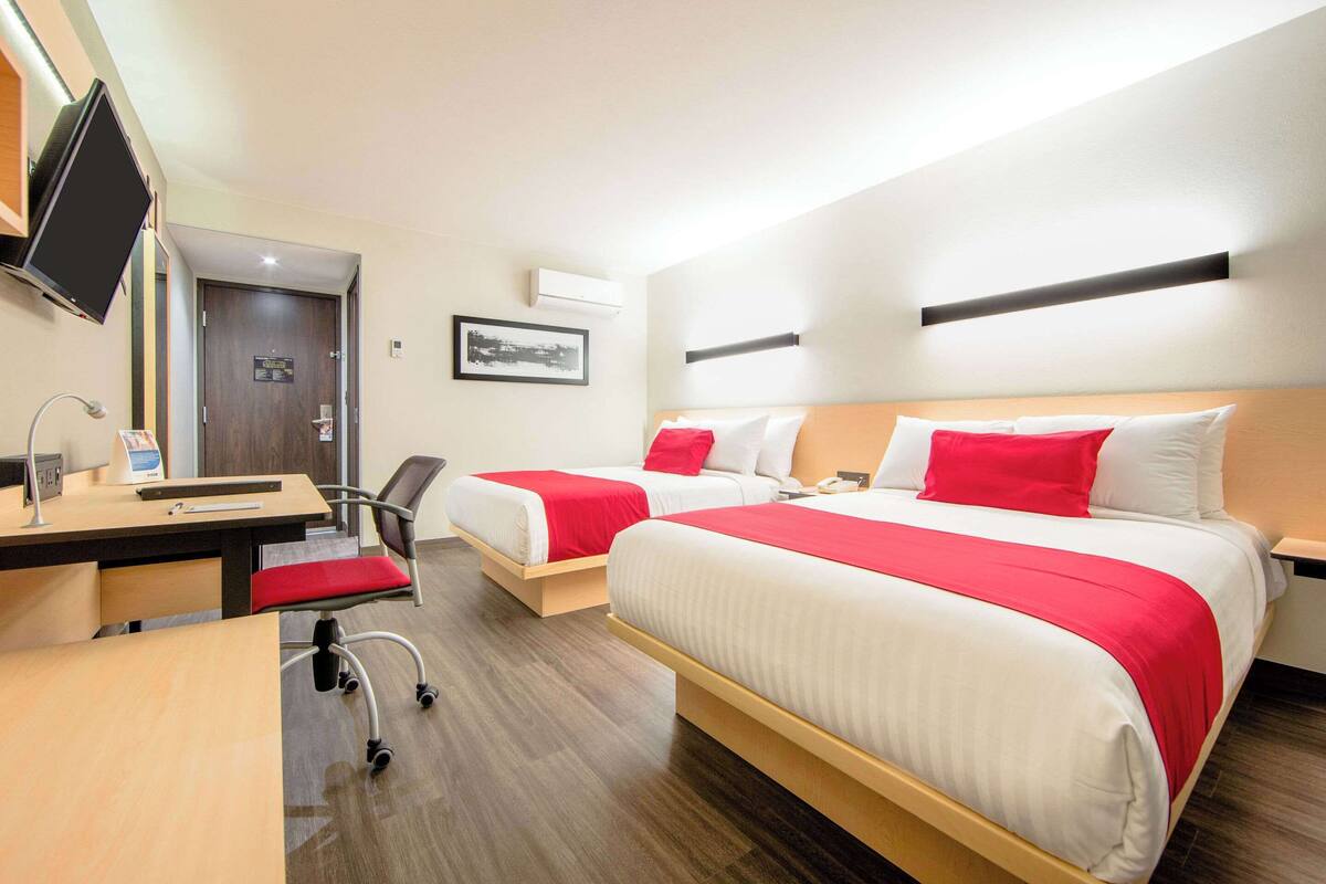 Ett hotellrum med två sängar, ett skrivbord, en stol, en TV och en dörr.