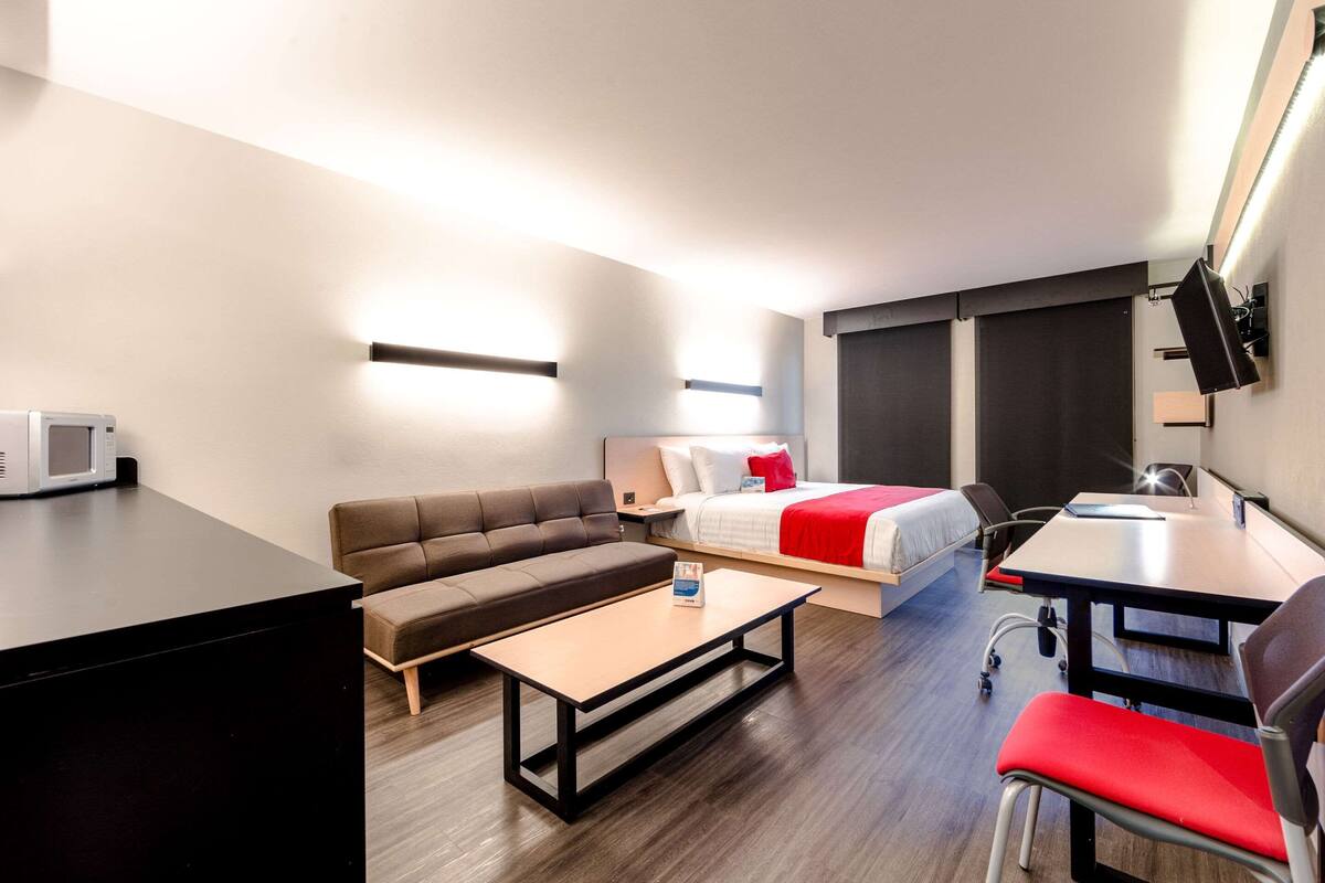 Ett modernt hotellrum med en soffa, en säng, ett skrivbord och en platt-TV.