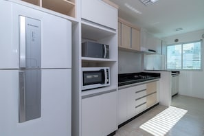 Cozinha moderna com armários brancos, micro-ondas embutido e fogão.