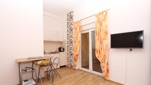 A compact room with a kitchenette, a desk with a chair, a bed, and a TV mounted on the wall. - SENA Studio with Balcony 1 (Rovinj)