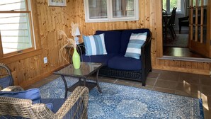 A cozy room with a blue sofa, wicker chairs, a glass coffee table, and a wooden floor.