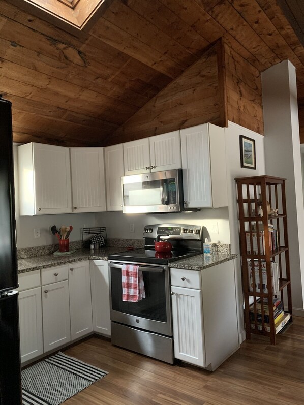 A compact kitchen with white cabinets, a stainless steel stove, and a microwave.