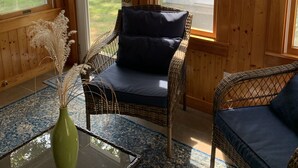 A cozy room with wicker furniture, a glass table, and a view of a white house through large windows.