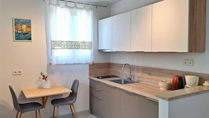 Een moderne keuken met een houten aanrecht, een spoelbak en kastjes. Er staat een eettafel met stoelen en een raam met gordijnen.