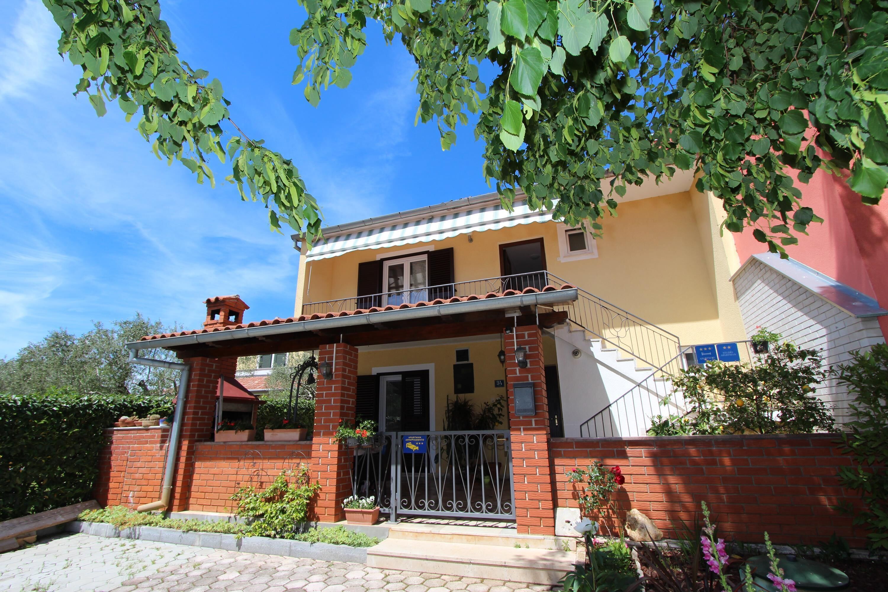 A two-story building with a balcony, a brick entrance, and a small garden area.