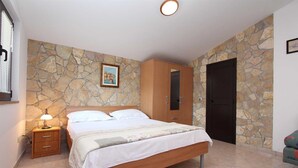 Un dormitorio con pared de piedra, una cama, un armario, una mesita de noche y una puerta.
