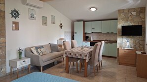 Una sala acogedora con un sofá, una mesa de comedor y sillas, una cocina con armarios verde claro, una pared de acento de piedra y un televisor montado sobre un mueble de madera.