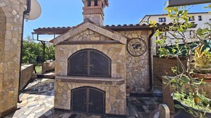 Cocina exterior de piedra con un reloj, rodeada de plantas en macetas y un suelo de baldosas.