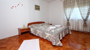 A bedroom with a wooden floor, a bed with a patterned bedspread, a nightstand with a lamp, and a painting on the wall. - GOGA Studio with Balcony 2 (Rovinj)