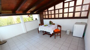 A covered patio with a table set for two, a refrigerator, and a view of greenery outside. - GOGA Studio with Balcony 2 (Rovinj)