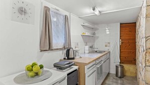 Cocina compacta con armarios blancos, un hervidor de acero inoxidable, una cafetera y un pequeño cubo de basura.