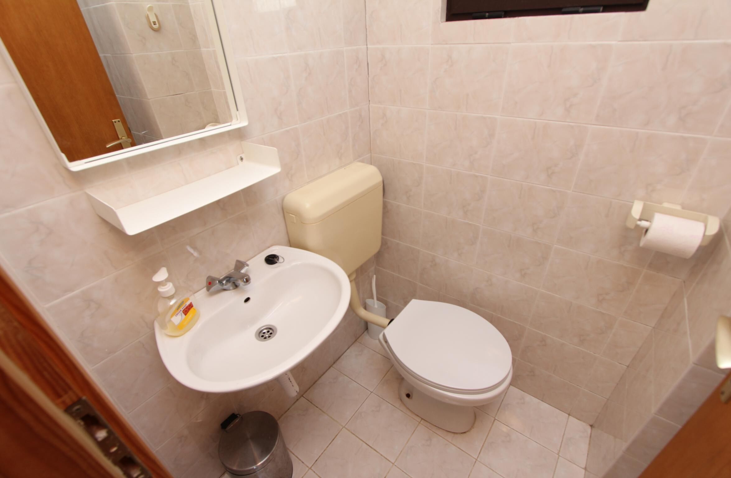 A small bathroom with a white sink, toilet, and mirror.