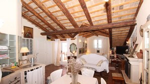 Een rustieke kamer met houten plafond, een bed, een eettafel met vaas en een keukenhoek met spoelbak en kastjes.