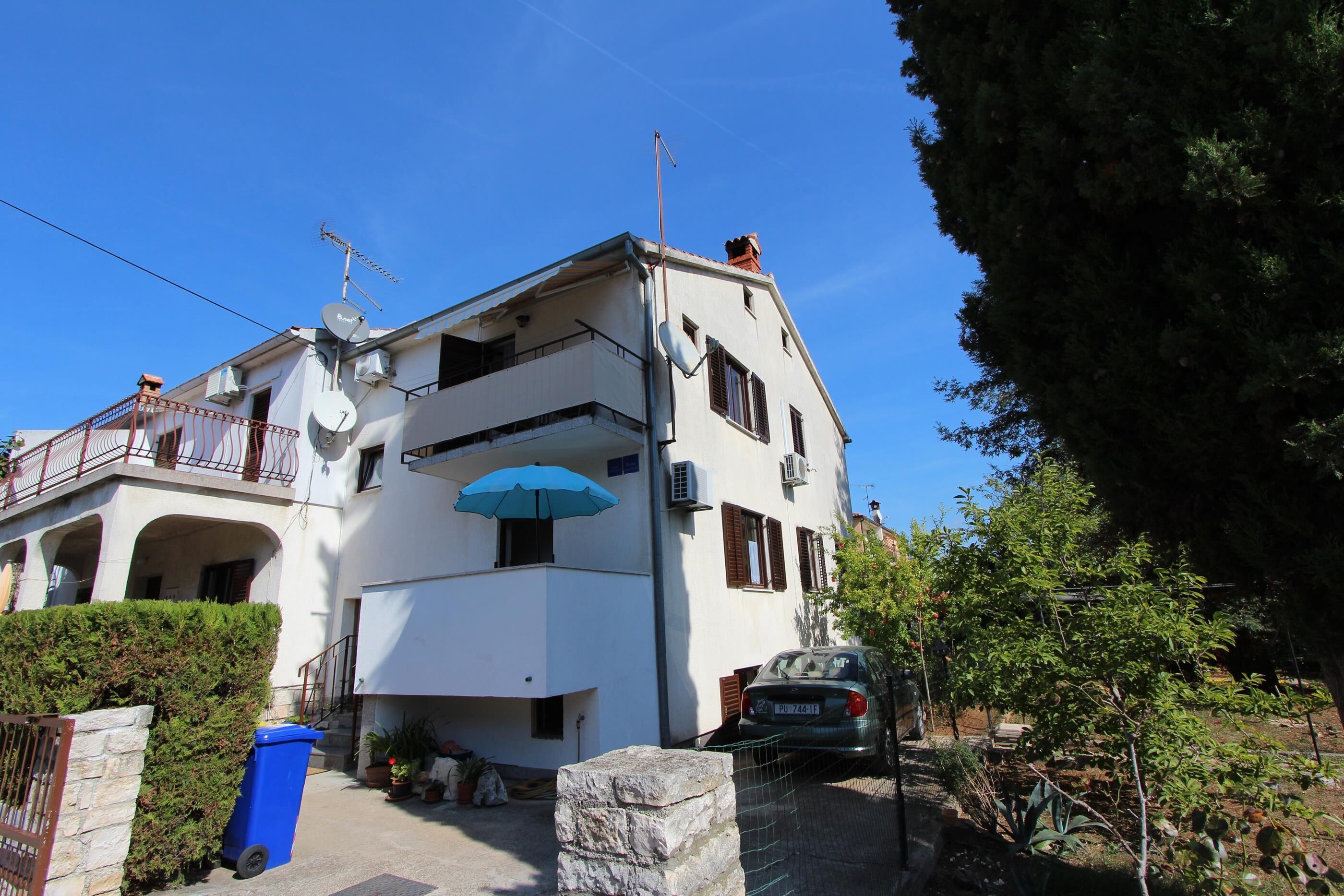 A two-story building with a balcony, satellite dishes, and a parked car.