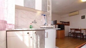 Uma cozinha compacta com geladeira embutida, micro-ondas e pia com torneira. Há uma pequena área de jantar com mesa e cadeiras.