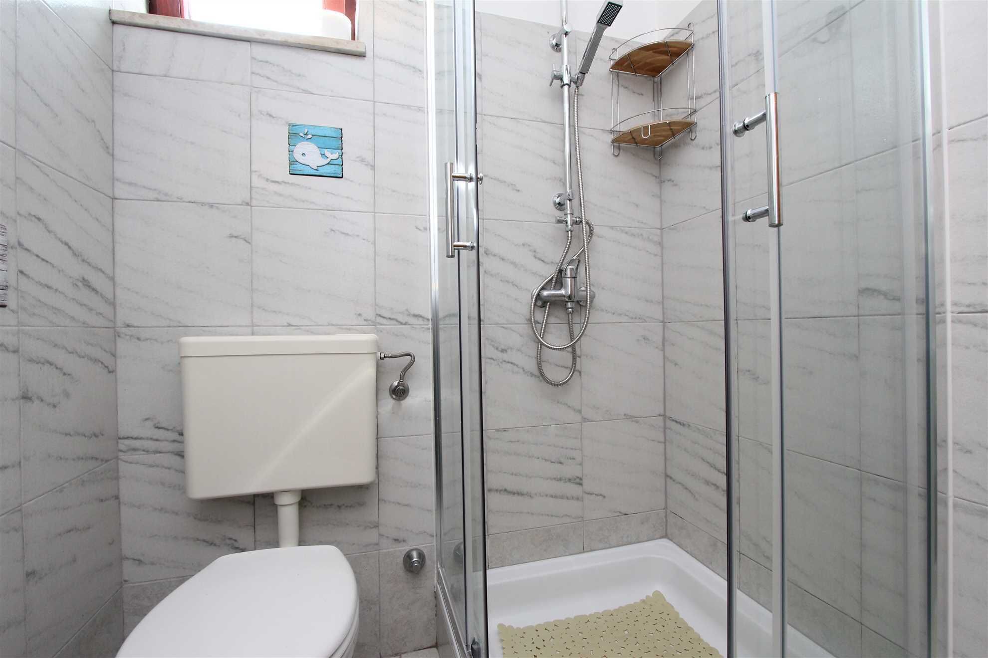 Ein modernes Badezimmer mit Duschkabine aus Glas, Toilette und einer kleinen Ablage für Pflegeprodukte.