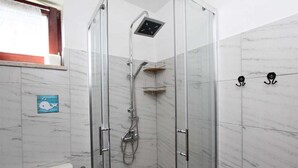 Um banheiro moderno com chuveiro em compartimento de vidro, banheira branca e parede revestida de mármore.