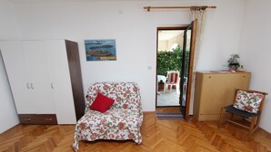 Et værelse med trægulv, en blomstret sofa, et lille skab og en dør til et udendørs område med et bord og stole.