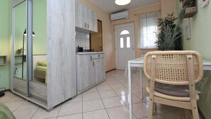 Een kleine keuken met een eethoek, een rieten stoel en een groot raam.