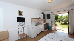 A compact room with a bed, a small kitchenette, a TV, and a sliding glass door to a garden. - ROSANNA Studio with Terrace (Rovinj)