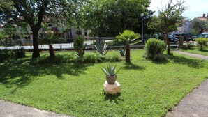 A well-maintained grassy area with a variety of plants and trees, a paved walkway, and a fence. - ROSANNA Studio with Terrace (Rovinj)