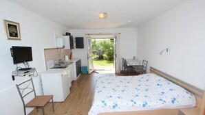 A bedroom with a bed, a desk, a chair, a television, a small kitchenette, and a sliding glass door leading to a garden. - ROSANNA Studio with Terrace (Rovinj)