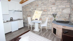 Une cuisine moderne avec des meubles blancs, un mur en pierre et un coin repas avec des chaises blanches.