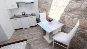 Une cuisine compacte avec des meubles blancs, un plan de travail et un mur en pierre. On y trouve une petite table avec une chaise blanche et un vase contenant des fleurs violettes.