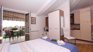 A hotel room with a bed, a chair, a small kitchenette, and a balcony with chairs and a table. - TANJA Studio with Balcony (Rovinj)