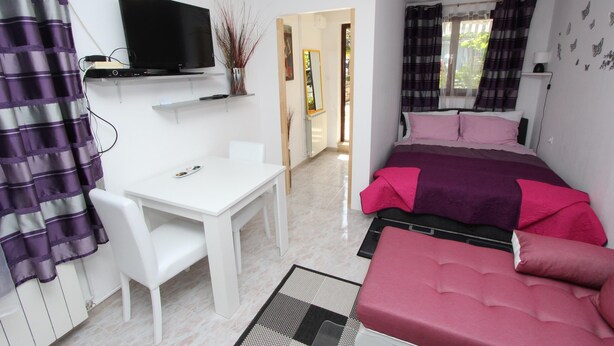 Une chambre à coucher avec un lit, un bureau, une télévision et une fenêtre avec des rideaux.
