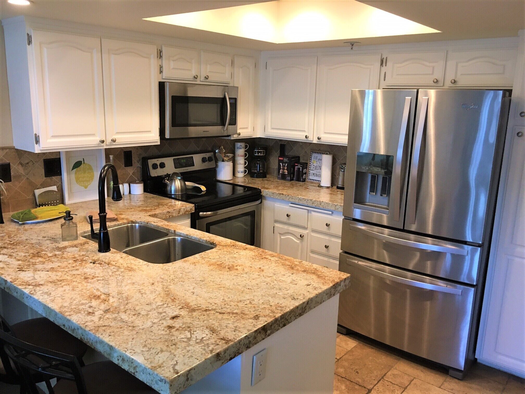 A modern kitchen with white cabinets, stainless steel appliances, granite countertops, and a double sink.