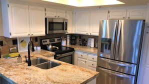 A modern kitchen with white cabinets, stainless steel appliances, granite countertops, and a double sink.