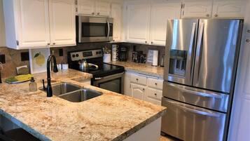 A modern kitchen with white cabinets, stainless steel appliances, granite countertops, and a double sink.