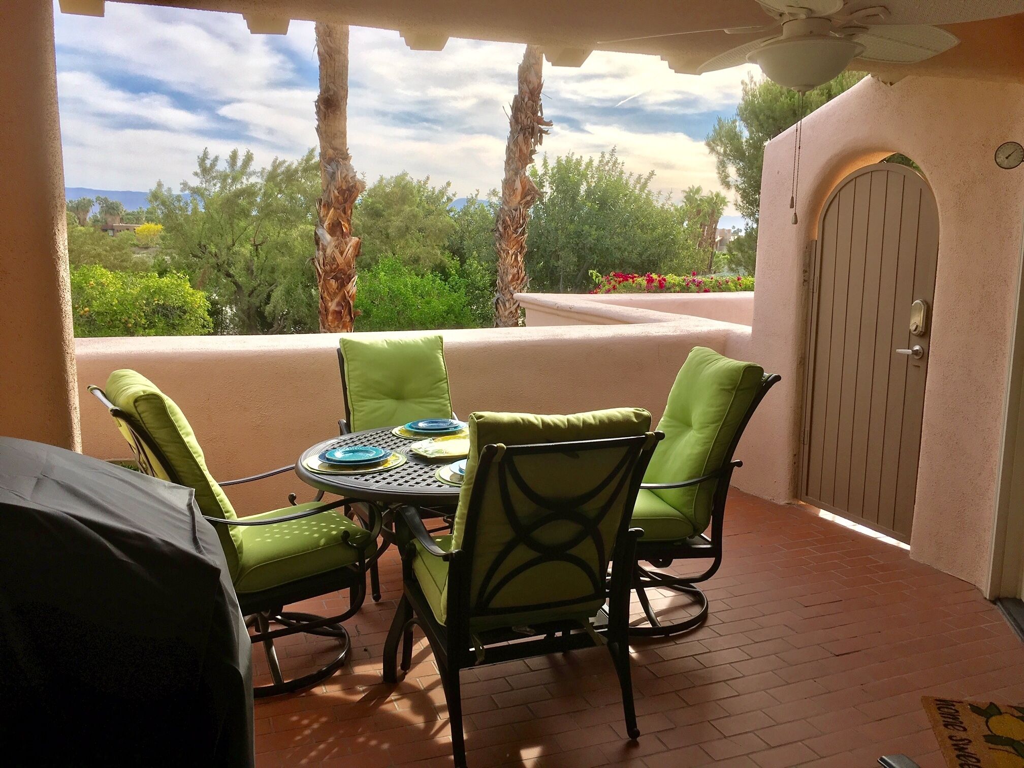 A patio with a round table and four chairs, a grill, and a door with a clock.