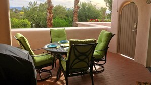 A patio with a round table and four chairs, a grill, and a door with a clock.
