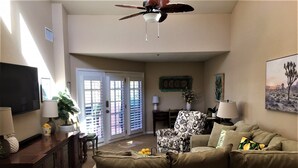 A living room with a sofa, a television, a ceiling fan, and a door with glass panels.