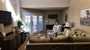 A living room with a sofa, a television, a ceiling fan, and a door with glass panels.