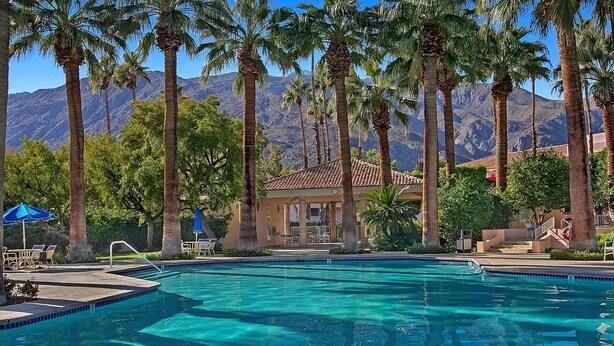 A swimming pool surrounded by palm trees and a mountain backdrop.