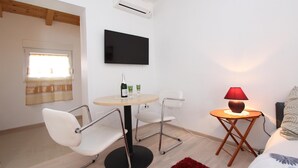 A modern room with a round table, two white chairs, a TV mounted on the wall, a small side table with a lamp, and a bed with a red rug. - SALLY Comfort Studio 6 (Rovinj)