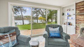 Un salon chaleureux avec une cheminée, une bibliothèque et une vue sur un lac, visible à travers de grandes portes-fenêtres coulissantes.