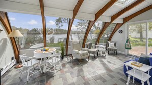 Une véranda avec vue sur un lac, comprenant une table blanche, des chaises et une plante en pot.
