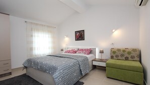 Un dormitorio con cama, mesitas de noche, una silla verde y una ventana con cortinas.