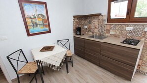 A small kitchen with a dining table and chairs, a painting on the wall, and a window above the sink. - MIDEA 2 Studio Apartment 4 (Rovinjsko Selo)