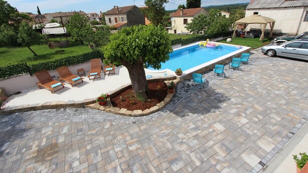A swimming pool with a tree in the center, surrounded by lounge chairs and a paved patio area. - MIDEA 2 Studio Apartment 4 (Rovinjsko Selo)