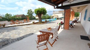 A covered patio area with a table and chairs, a small tree, and a swimming pool in the background. - MIDEA 2 Studio Apartment 4 (Rovinjsko Selo)