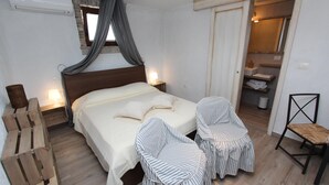 A bedroom with a large bed, two striped chairs, a wooden bench, a small table, and a bathroom visible through an open door. - MIDEA 2 Studio Apartment 4 (Rovinjsko Selo)