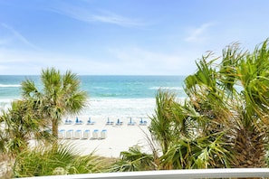 Blick auf einen Strand mit weißem Sand, Meereswellen und blauem Himmel. Palmen und blaue Liegen sind zu sehen.