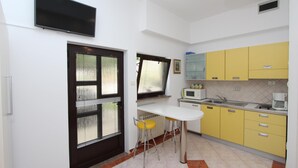 A compact kitchen with a white countertop, yellow cabinets, a black-framed window, and a flat-screen TV mounted above the counter.