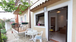 A small patio with a table and chairs, a balcony with potted plants, and a glimpse of the interior.